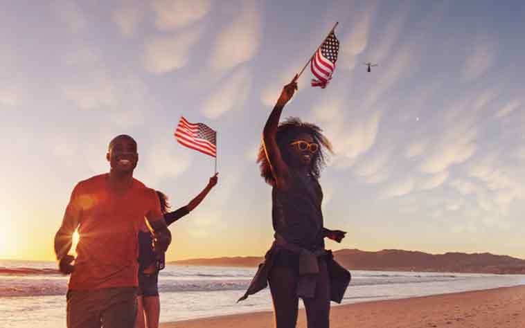 Young African American man and woman waving American flags and considering July 4th safety tips.
