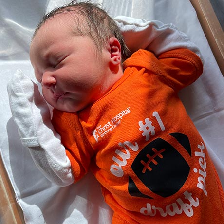 Newborn wearing orange football onesie reading 