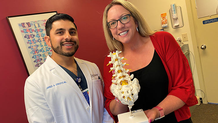 Jared Crasto, MD, and Q102's Jennifer Fritsch hold a model of the lumbar spine