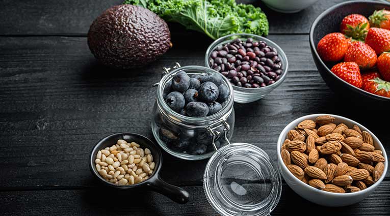 Fruits, nuts, and kale on a dark wood table