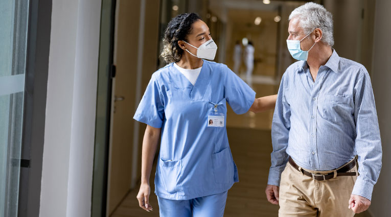 Healthcare worker guides older male patient through hospital corridor