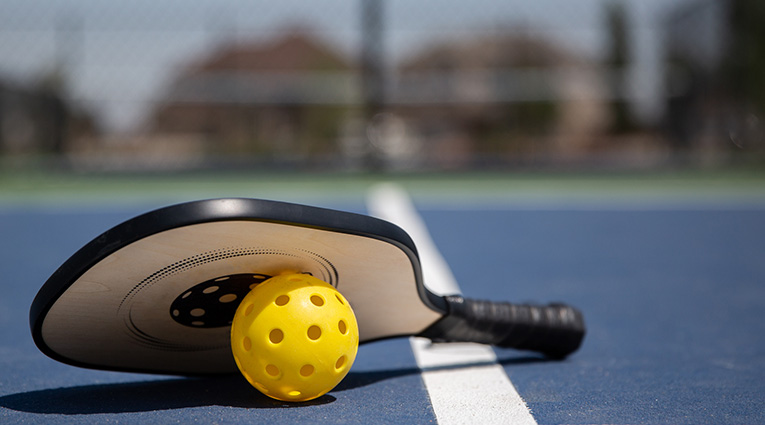 Pickleball and paddle laying on court