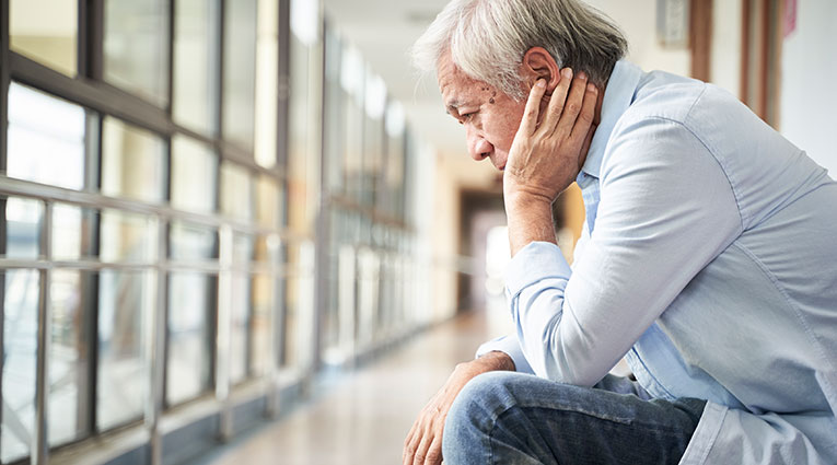 Older man sits in deep thought in medical office hallway