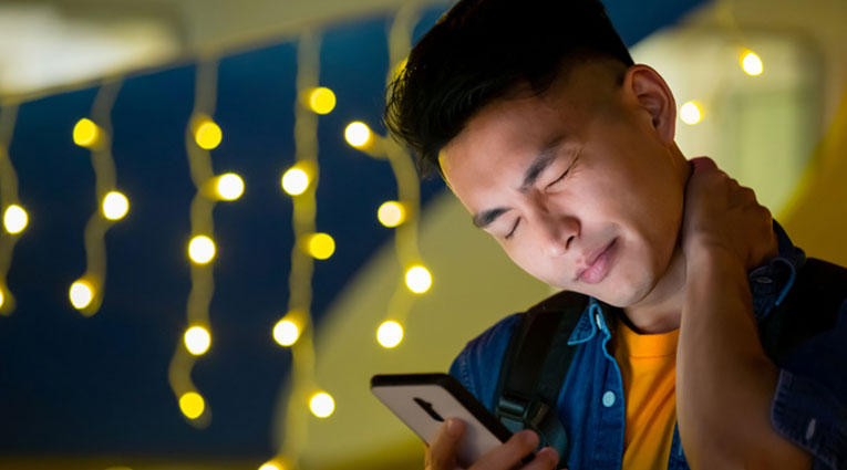 man looks at cell phone while rubbing sore neck