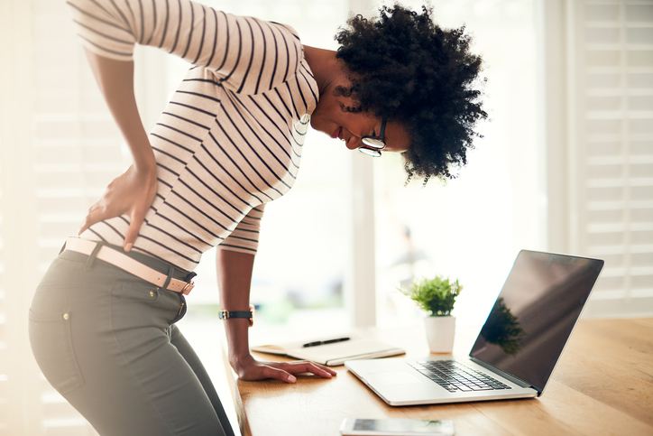 Young black woman bending over with back pain while working from home.