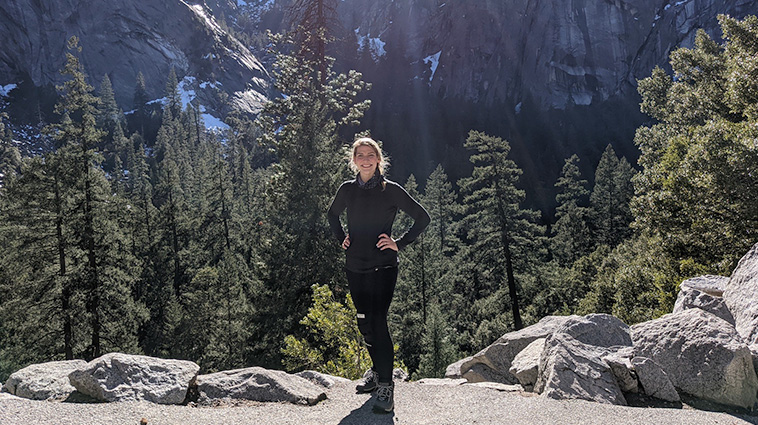 Cara Shultz wears black hiking gear as she hikes a mountain after knee replacement surgery. 