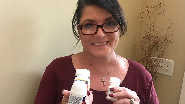 B105 radio personality Chelsie smiling and wearing a burgundy top while holding headache medicine for her blog on migraines.