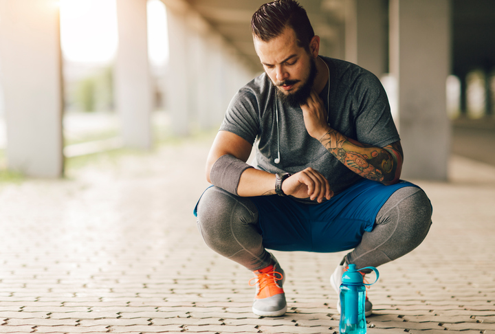 Caucasian male with beard checking his heart rate during exercise outdoors.