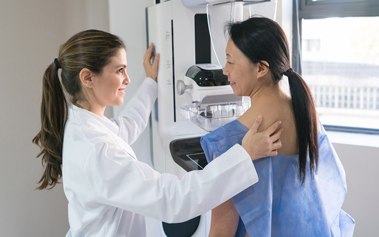 Woman stands at mammogram machine with healthcare worker.