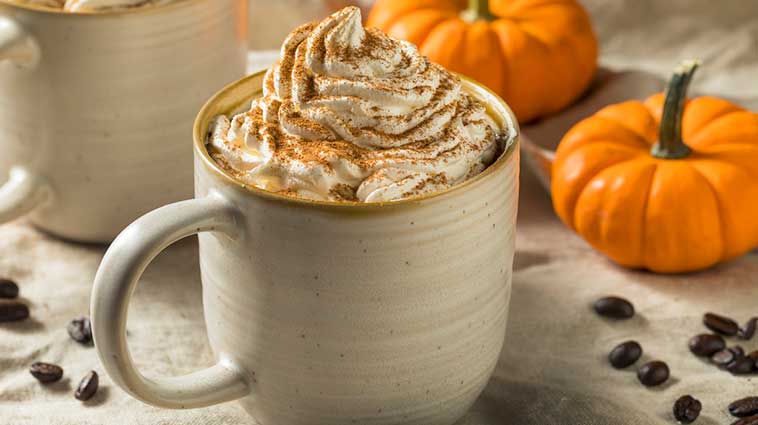 A healthier pumpkin spice latte, surrounded by miniature pumpkins.