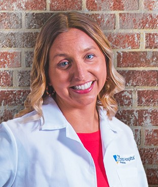 Leanne Olshavsky, MD, wearing a white lab coat and standing in front of a brick wall.