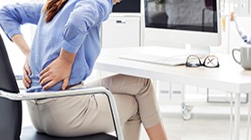 Woman sitting at desk holding back