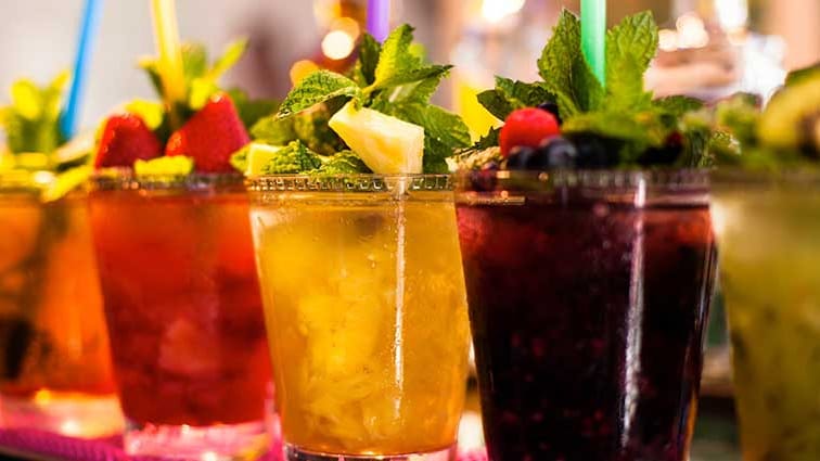 A line of multi-colored iced beverages with garnish on top.