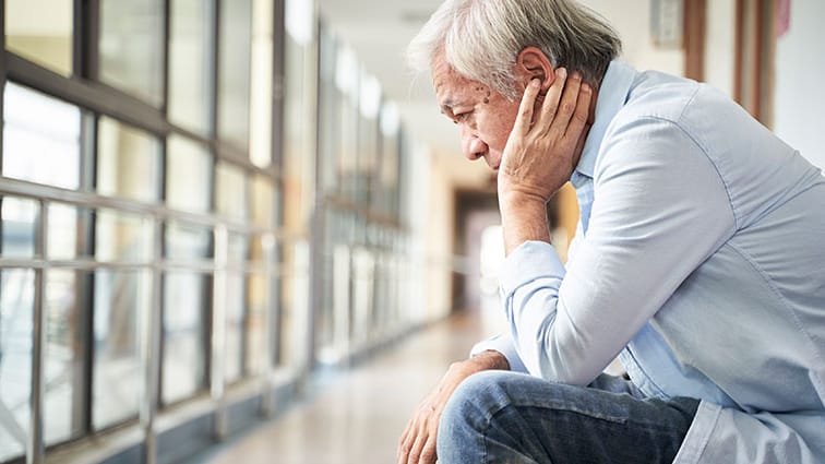 Older man sits in deep thought in medical office hallway