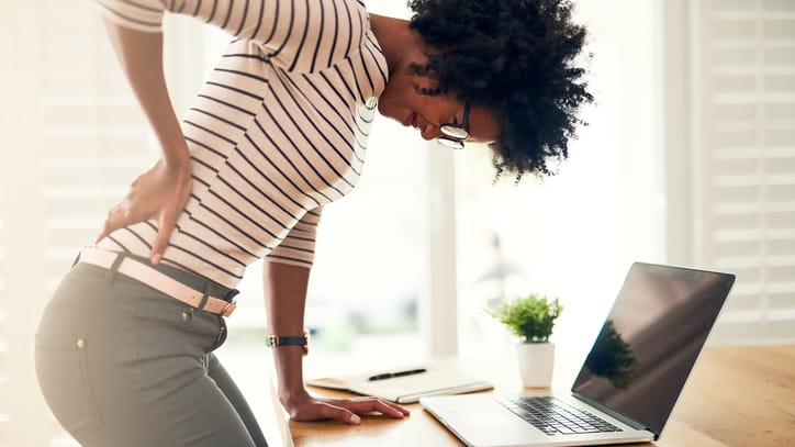 Young black woman bending over with back pain while working from home.