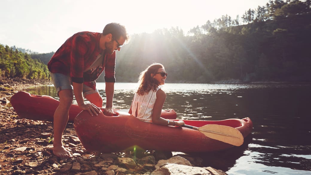 A man and woman in a canoe on the edge of water, practice water safety.