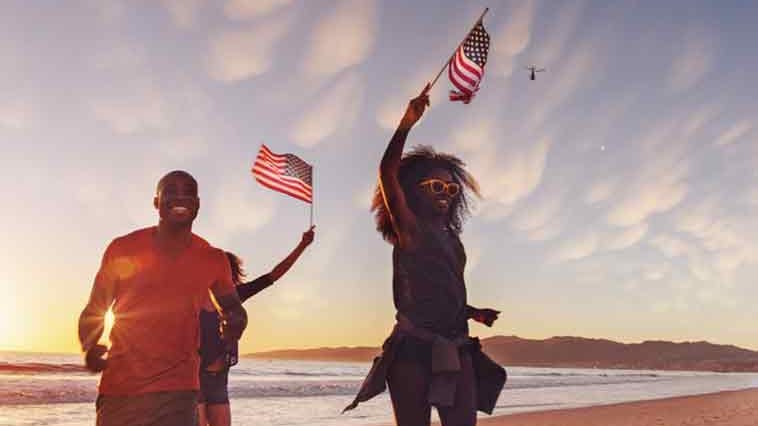 Young African American man and woman waving American flags and considering July 4th safety tips.