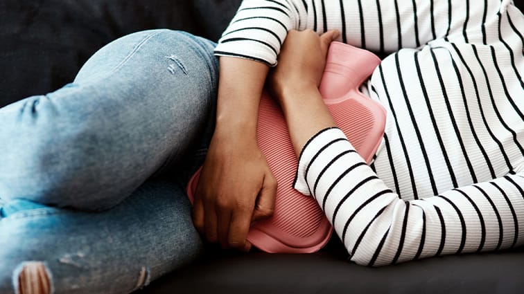 Woman experiencing pelvic pain holds hot water bottle
