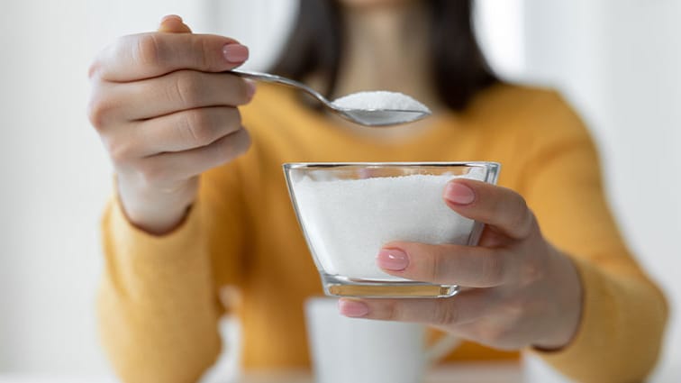 Person holding sugar bowl and taking out a heaping spoonful of sugar