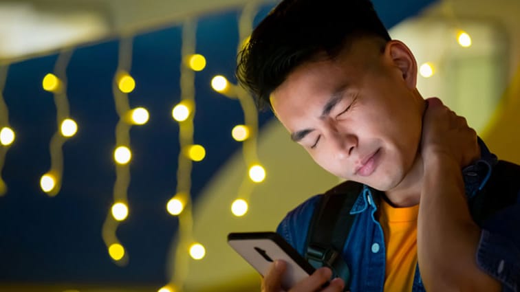 man looks at cell phone while rubbing sore neck
